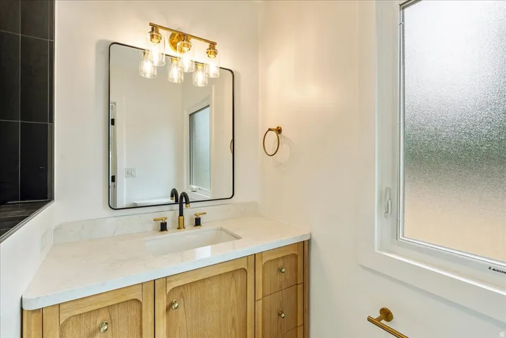 Spa-inspired bathroom vanity featuring warm wood-finish cabinetry, a marble-look countertop, and brushed brass hardware