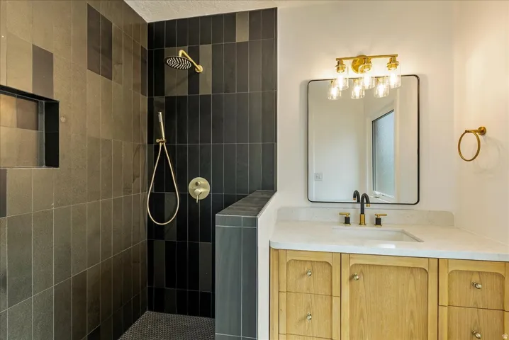 Spa-inspired primary bathroom featuring a walk-in shower with black tile surround, rainfall showerhead, and hand shower