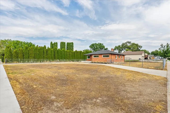 Expansive lot featuring a brick structure with a dark roof, surrounded by mature trees and a chain-link fence