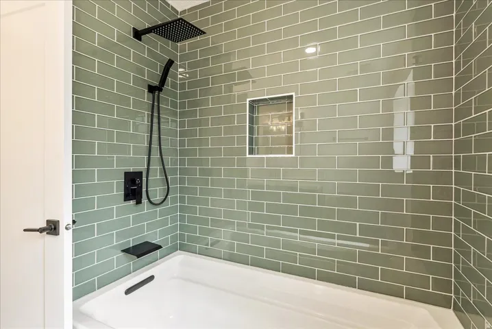 Bathtub with sage green subway tile surround, matte black shower fixtures, a built-in shower niche,