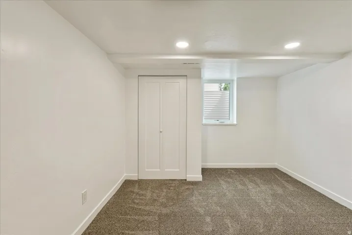 Recessed lighting, white bi-fold closet doors, white walls, gray textured carpeting, and a window
