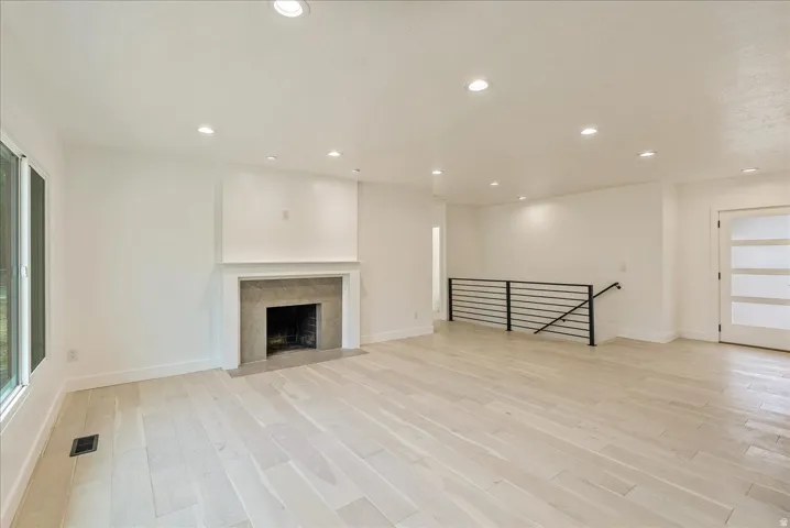 Bright open-concept living space featuring wood-finish flooring, recessed lighting, and a tile-surround fireplace with a classic mantel