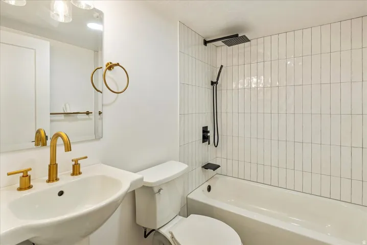 Pedestal sink with gold-tone fixtures, wall-mounted mirror, white subway tile shower surround, integrated bathtub, and matte black shower system