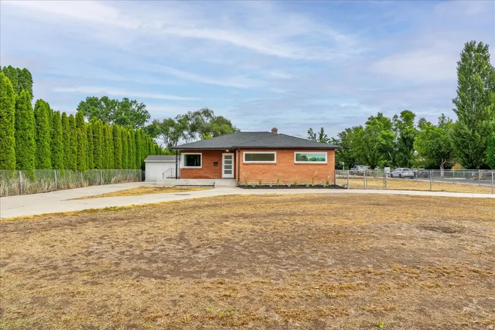 Modern single-story residence with warm brick and wood-finish exterior, situated on an expansive cleared lot