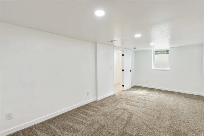 Bright, versatile room featuring fresh white walls, recessed ceiling lighting, neutral carpet flooring, and a large window allowing natural light