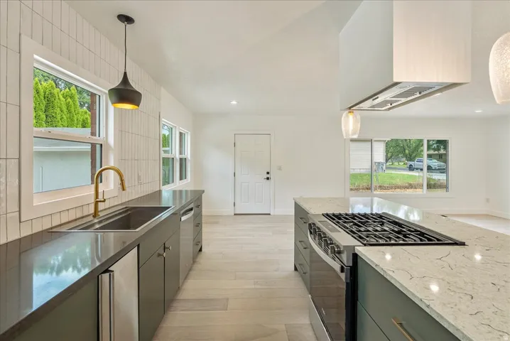 Sleek kitchen with stainless steel appliances, a gas range, white tile backsplash, and light wood-finish flooring