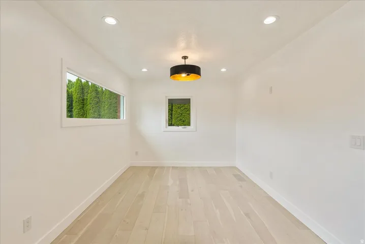 Bright, light-filled room featuring pristine wood-finish flooring, recessed ceiling lighting, and a modern pendant fixture with black and brass accents