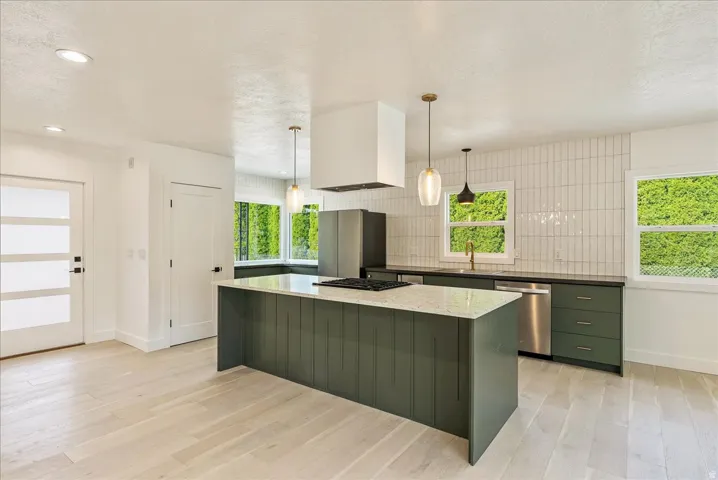 Kitchen featuring light wood-finish flooring, a center island with a light-toned countertop, a tile backsplash, and dark cabinetry