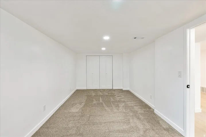 Spacious carpeted bedroom with neutral wall finishes, recessed ceiling lighting, and a large closet
