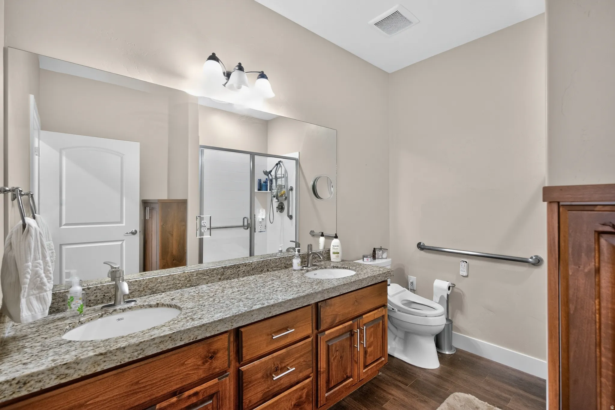 Spa-inspired primary bathroom featuring a wood-finish vanity with dual sinks, granite countertop, and polished chrome fixtures