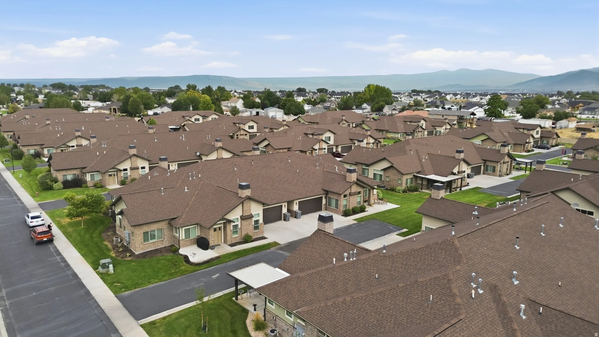 Aerial view of a well-planned residential community featuring multiple single-family homes with brown architectural roofing, manicured lawns, and organized street layout