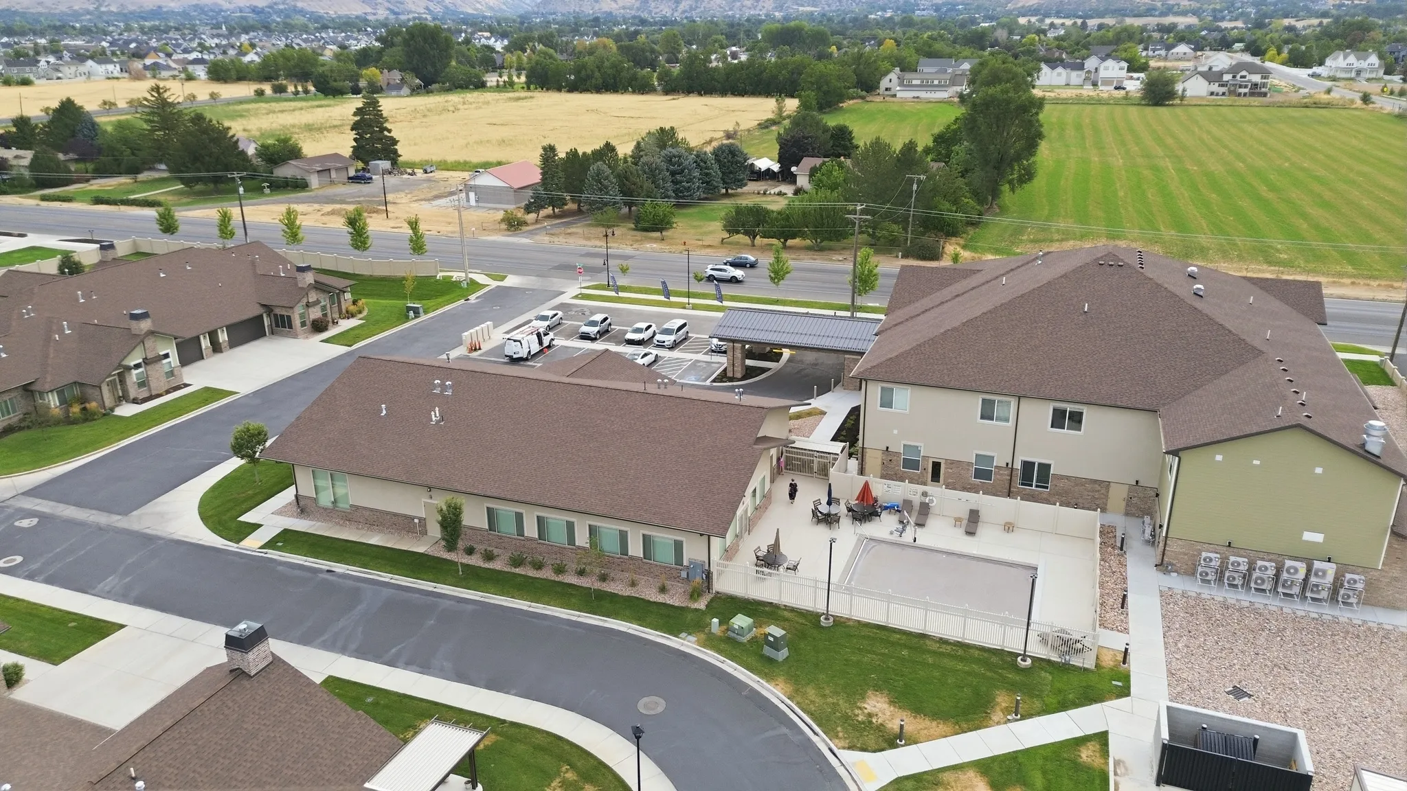 Aerial view of a contemporary two-story residential property featuring a dark-shingled roof, light-colored exterior siding, and a curved driveway with parking area