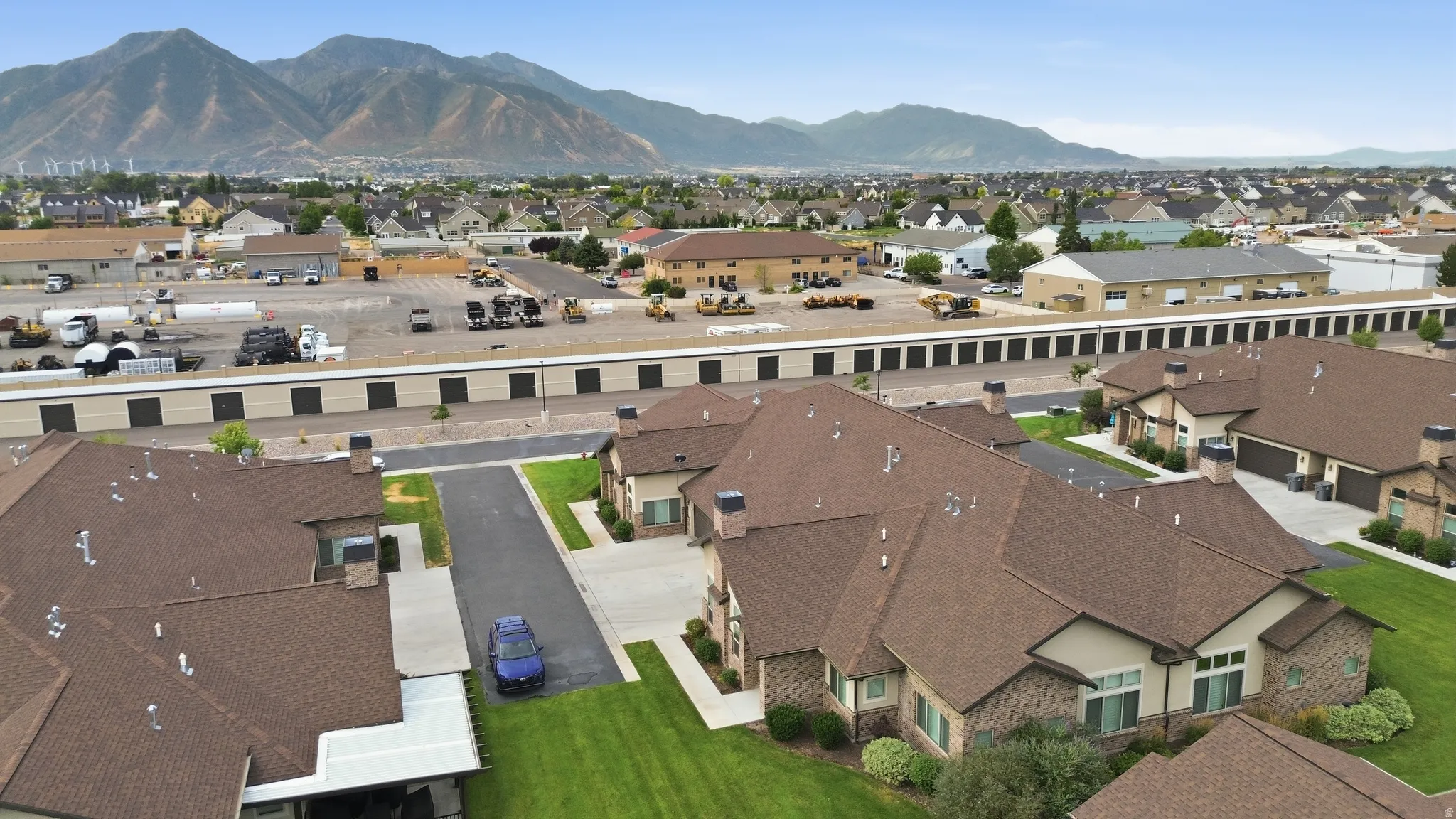 Aerial view showcasing a brick and stone residence with a dark asphalt shingle roof, situated on manicured landscaping with mature lawn
