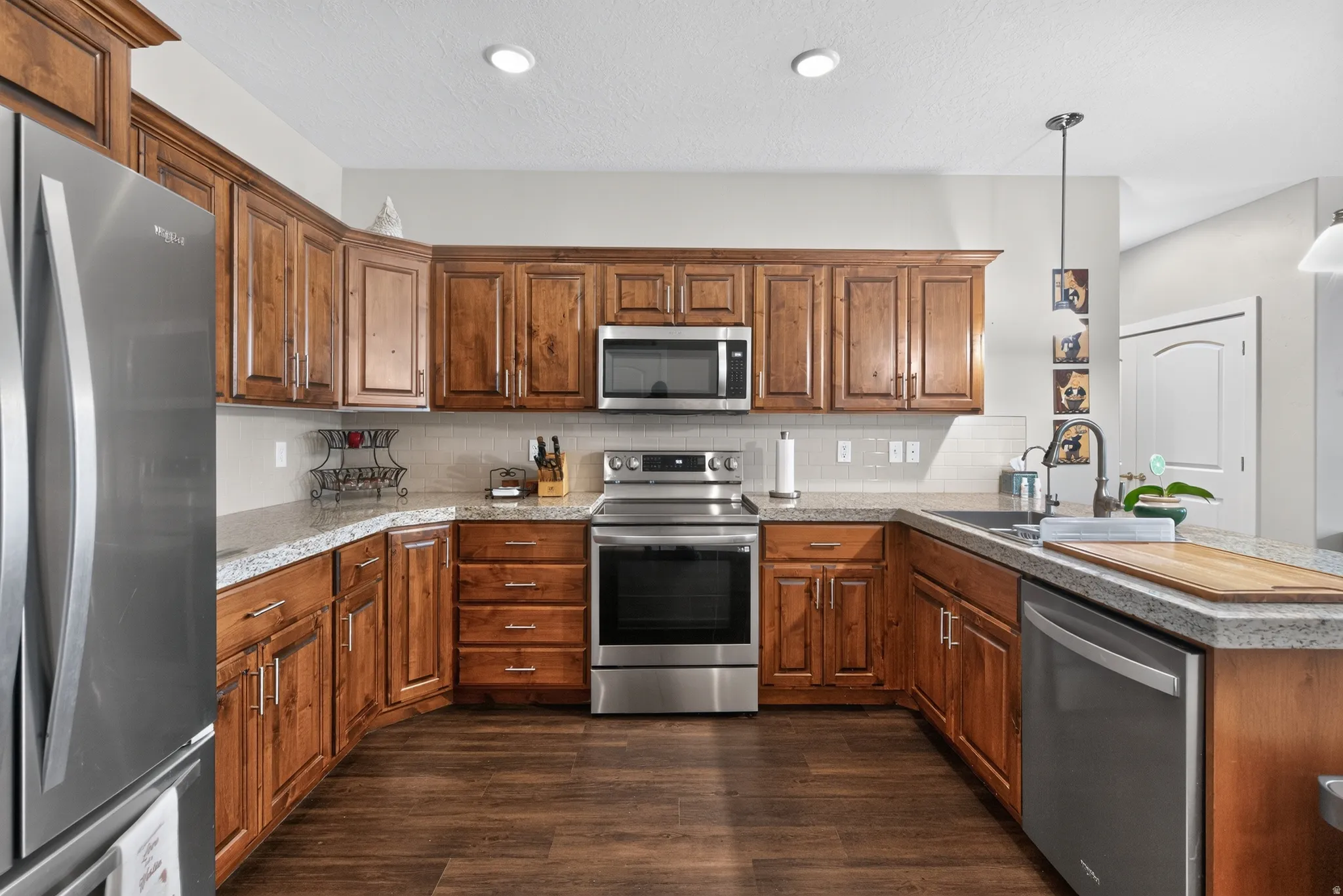 Chef's kitchen featuring warm wood cabinetry throughout, stainless steel appliances including a gas range and built-in microwave, wood-finish flooring, and a spacious island with countertop seating