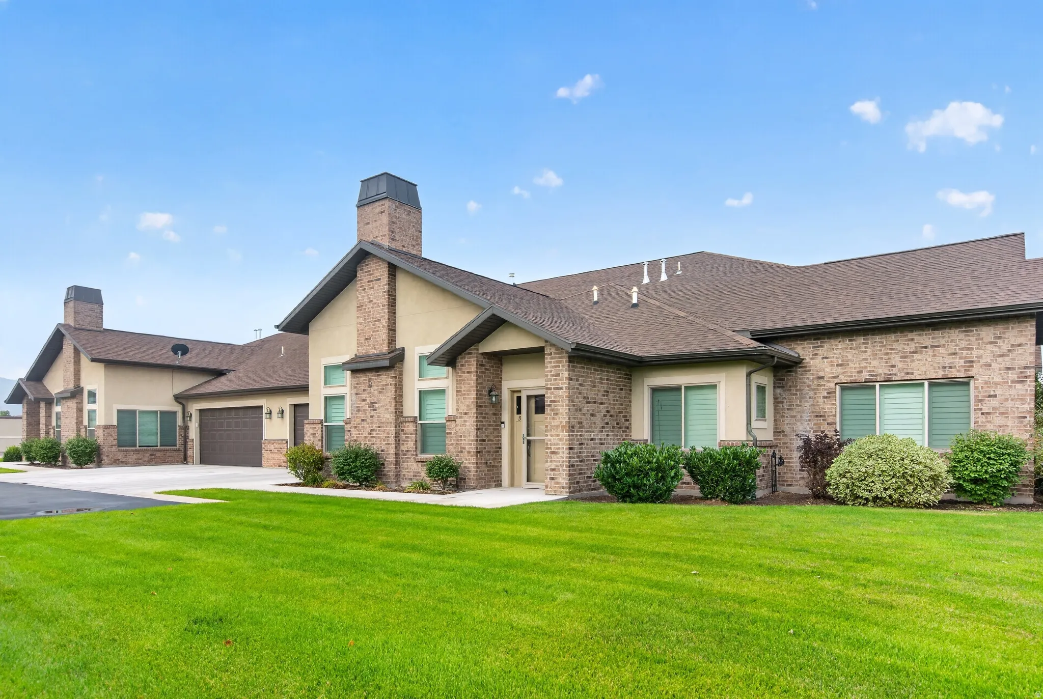 Elegant brick and stone residence featuring a gabled roofline with multiple chimneys, arched entryway, and coordinating stucco and masonry exterior
