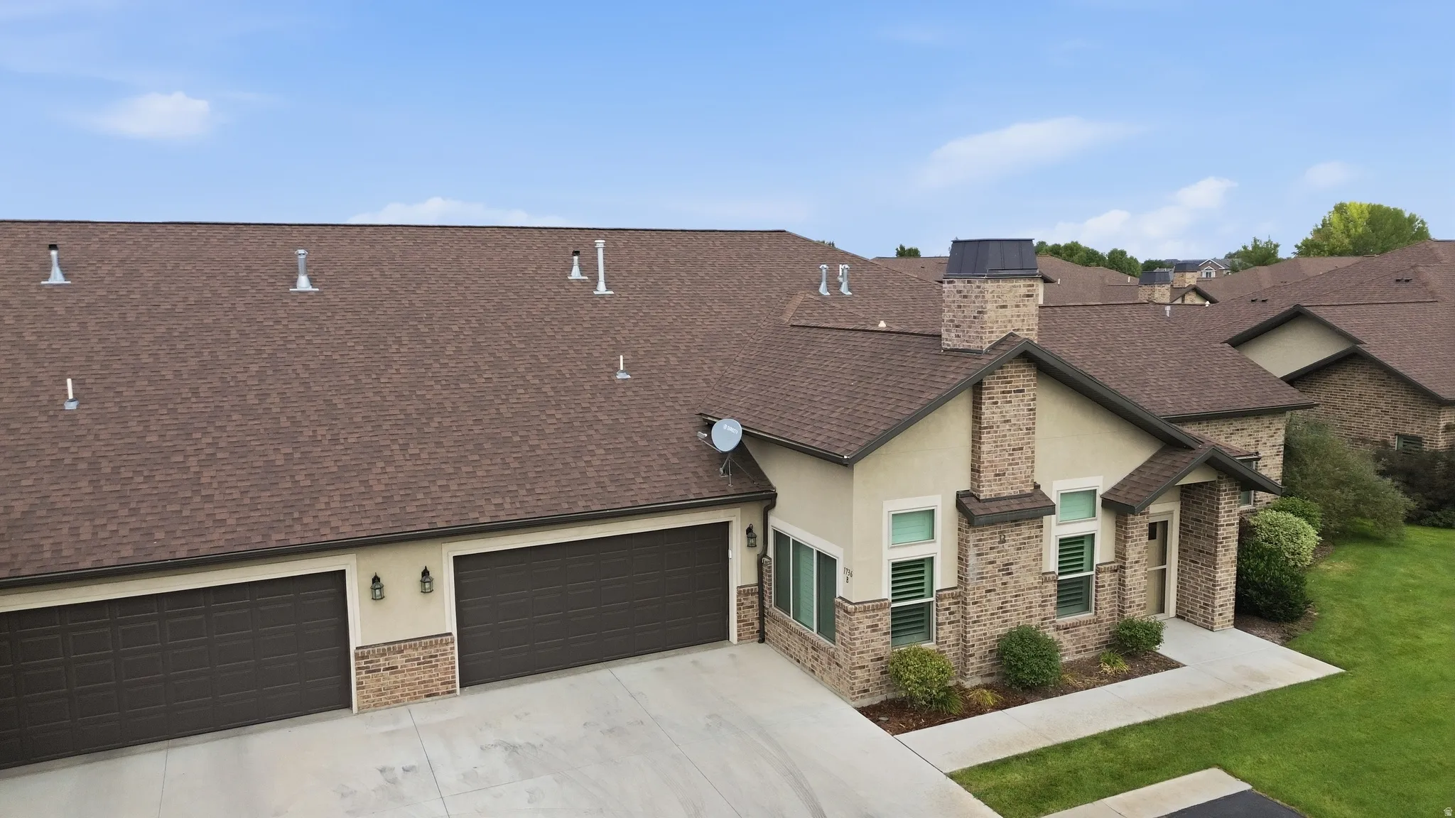 Multi-pitched shingle roof, stone and stucco exterior, prominent brick chimney, two-car garage with carriage-style doors, and well-maintained landscaping