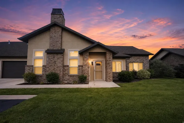Brick and stucco exterior, prominent brick chimney, dark shingle roofing, attached two-car garage, and established landscaping