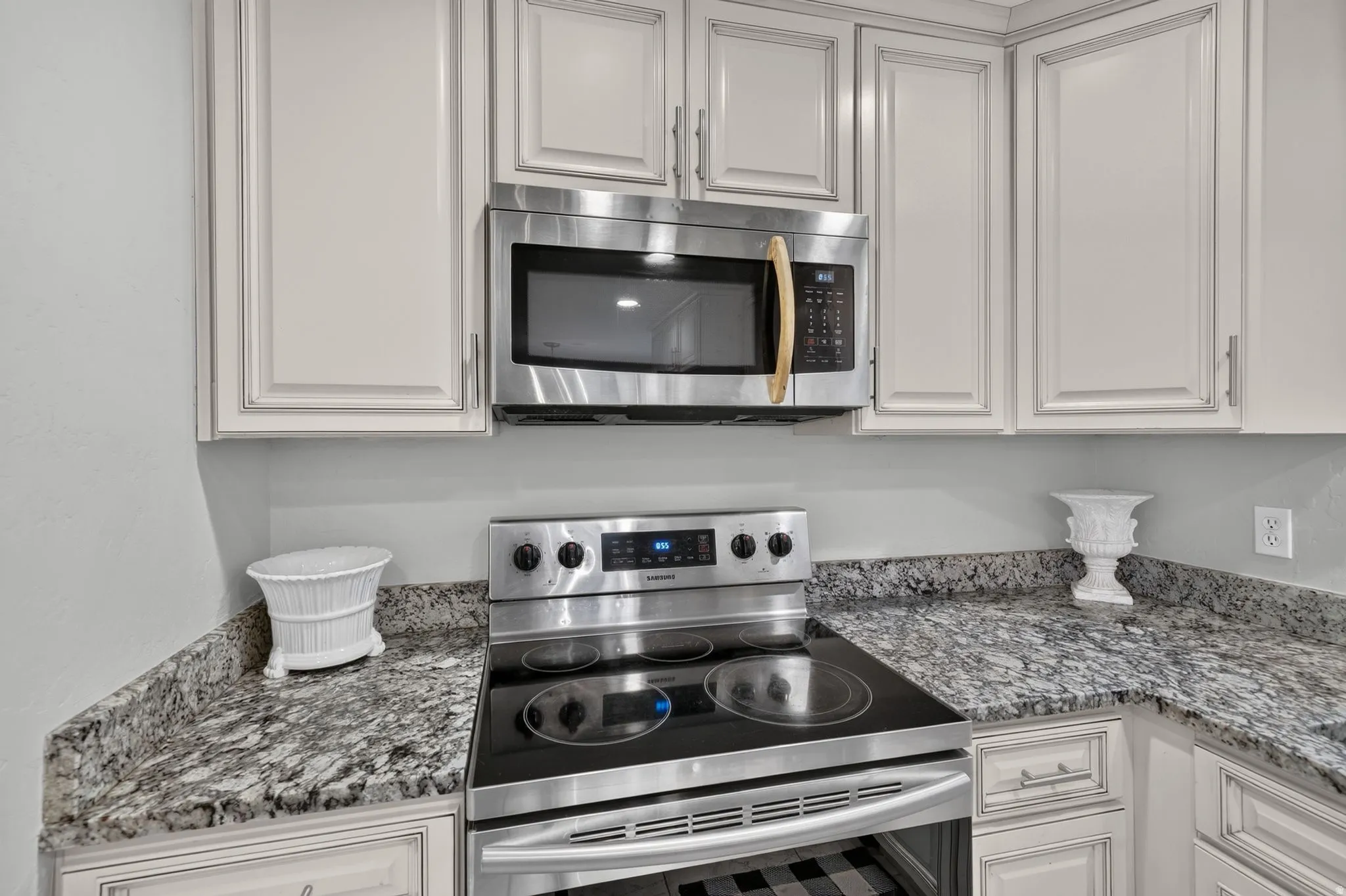 Modern kitchen featuring stainless steel appliances including a slide-in electric range and over-the-range microwave, speckled gray quartz countertops, crisp white cabinetry with contrasting trim detail, and brushed nickel hardware throughout