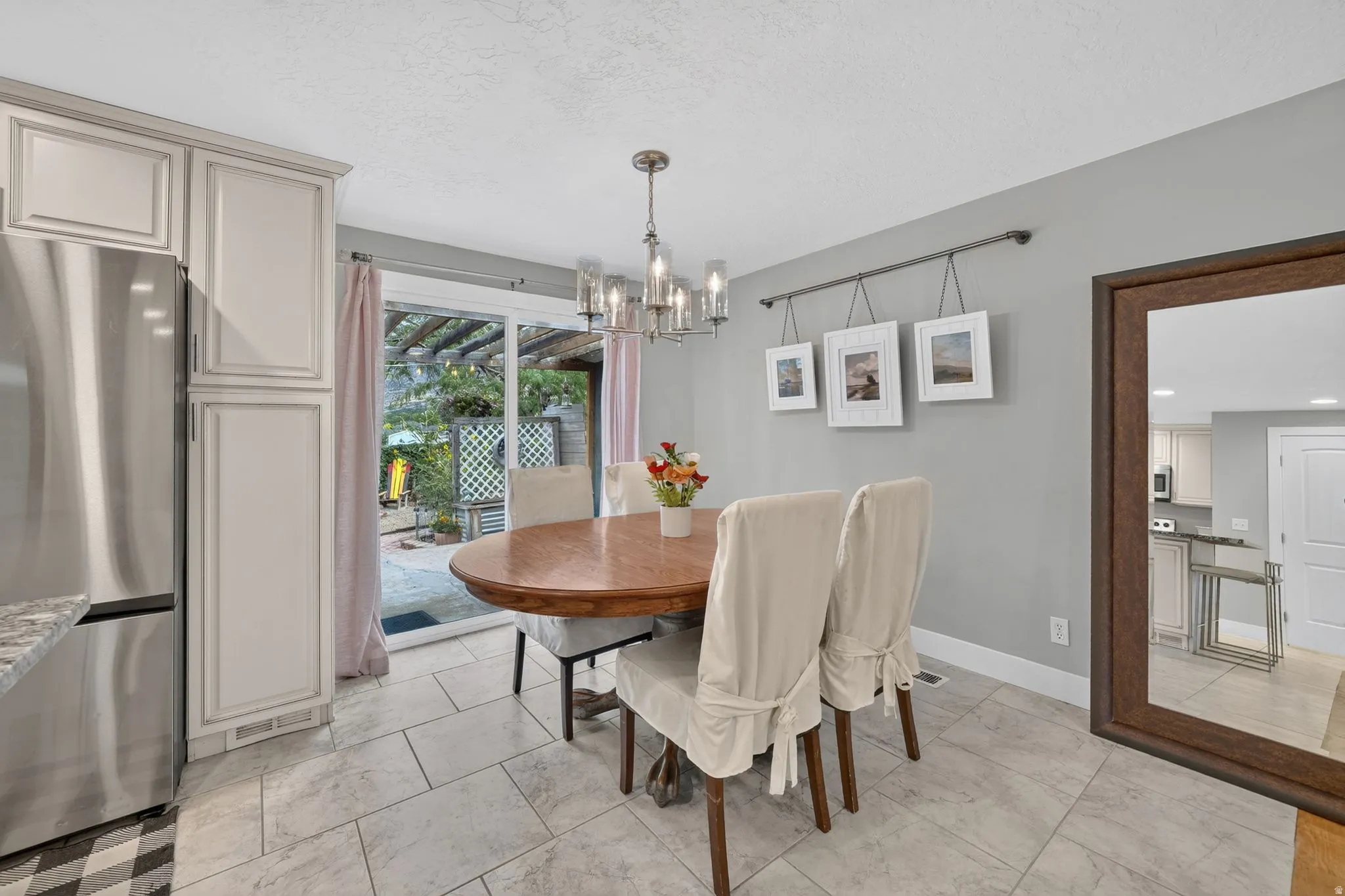 Bright dining area with wood-finish table, neutral tile flooring, and abundant natural light from French doors opening to the backyard