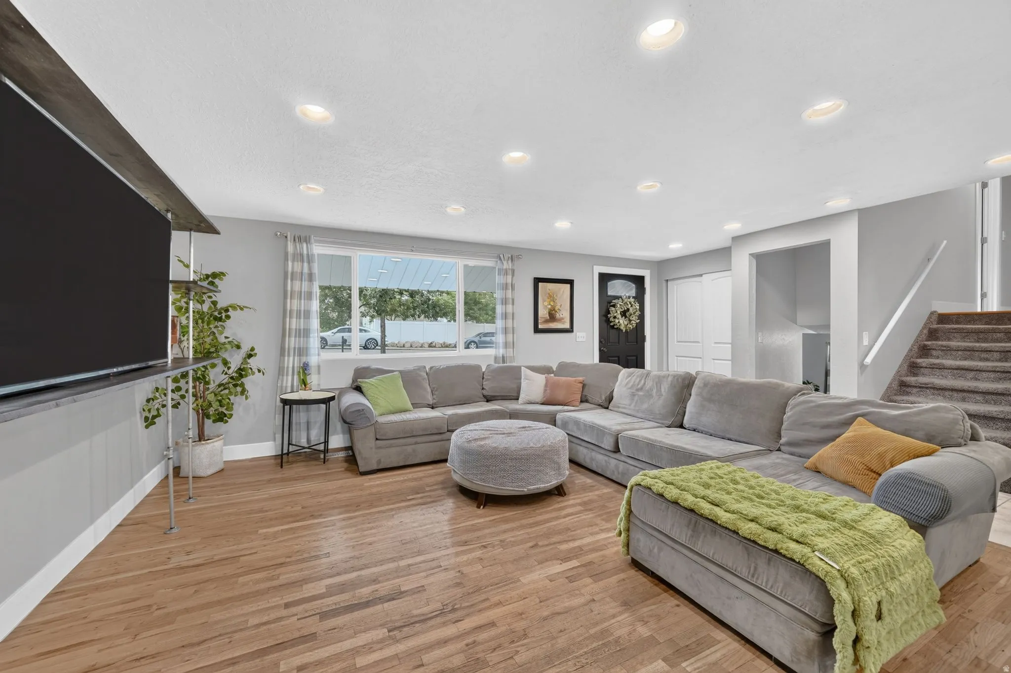 Spacious open-concept living area featuring a wood-finish plank floor, recessed ceiling lighting, and abundant natural light from large multi-pane windows