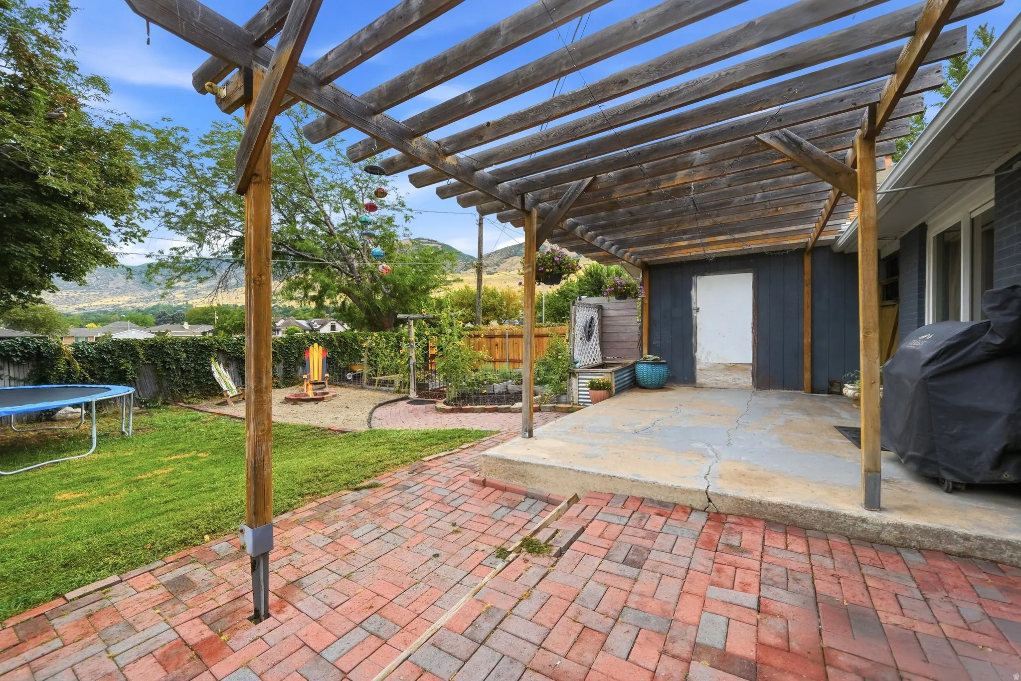 Expansive brick patio with wood-beam pergola overhead, offering defined outdoor entertaining space