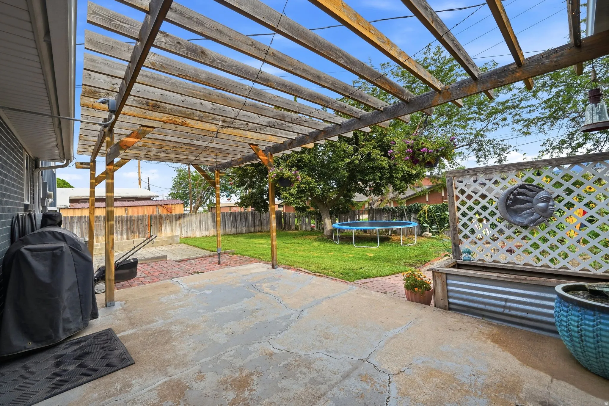 Expansive backyard oasis featuring a wooden pergola with polycarbonate panels, mature landscaping, level stone patio, manicured lawn, and detached storage structure