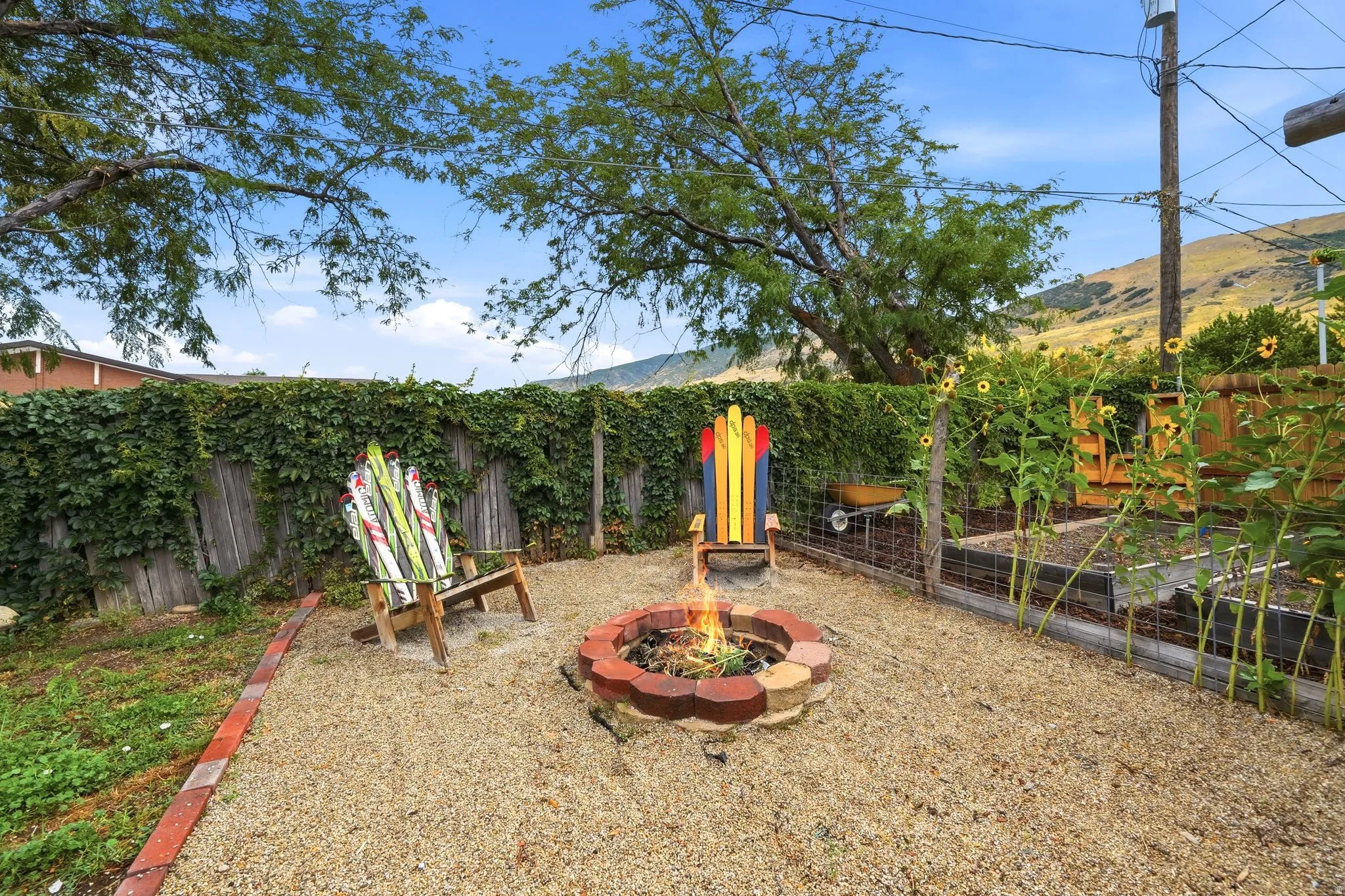 Outdoor entertaining space featuring a circular fire pit with metal surround, gravel foundation, and Adirondack-style seating