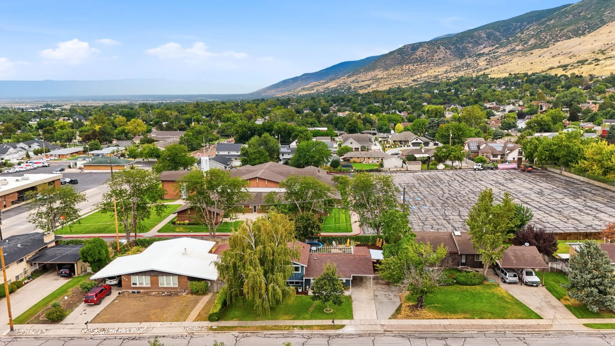 Aerial view showcasing a residential property with mature landscaping, established trees throughout the grounds, and a maicured lawn