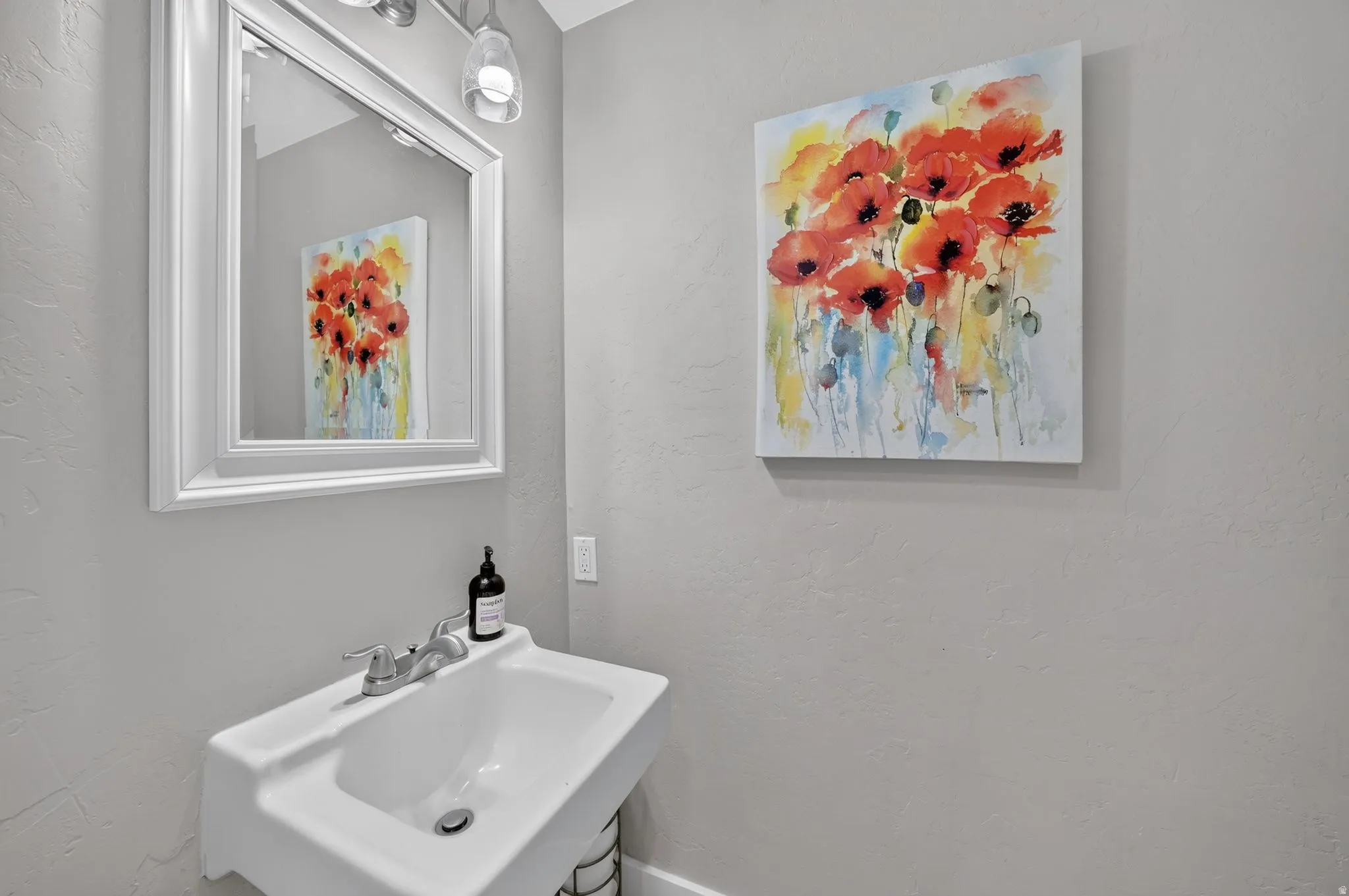 Elegant powder room featuring a white rectangular vessel sink with polished chrome faucet and fixtures, soft gray walls, framed mirror with chrome surround, and watercolor floral artwork
