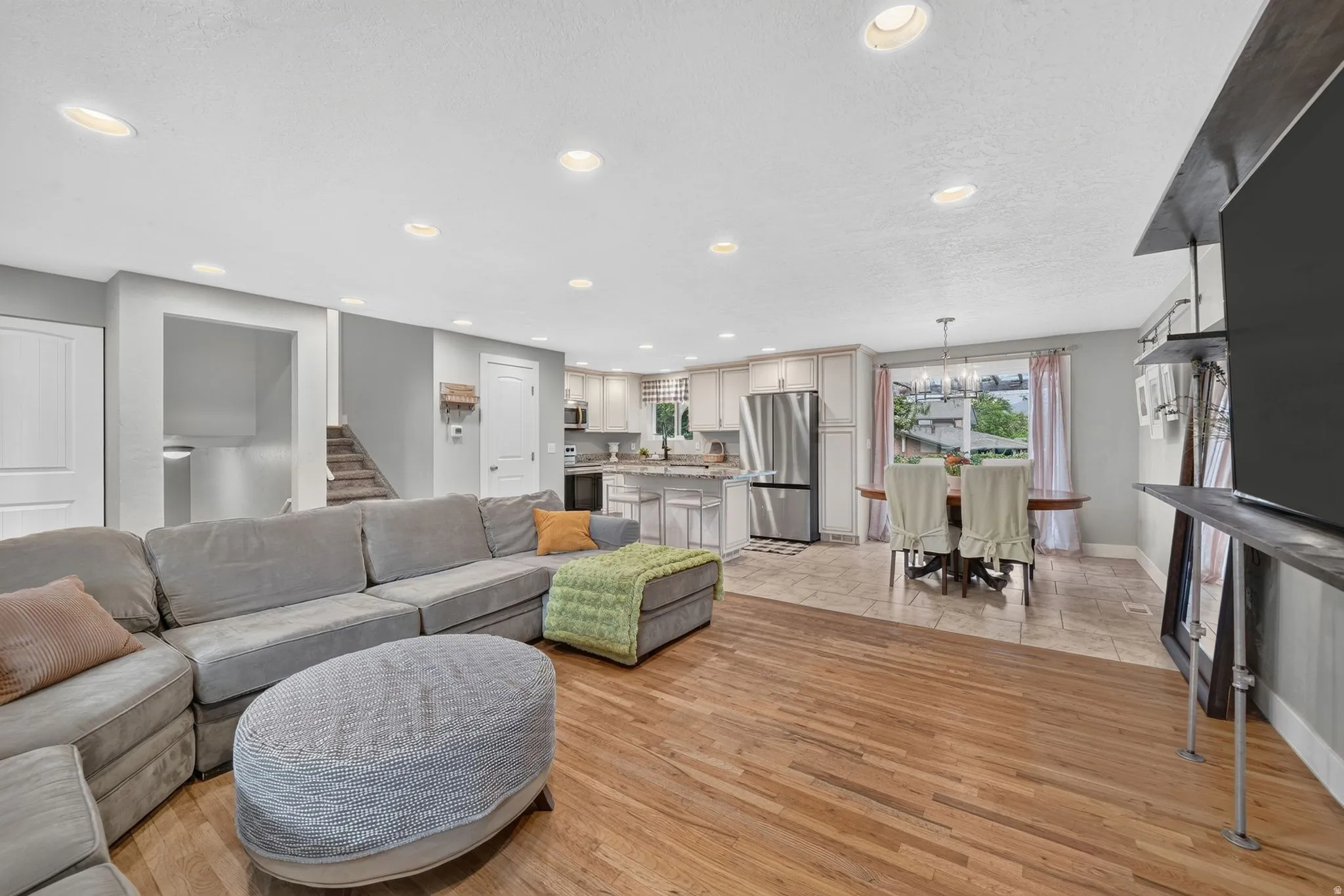Open-concept living area featuring a curved sectional sofa arrangement, wood-finish flooring throughout, and recessed ceiling lighting