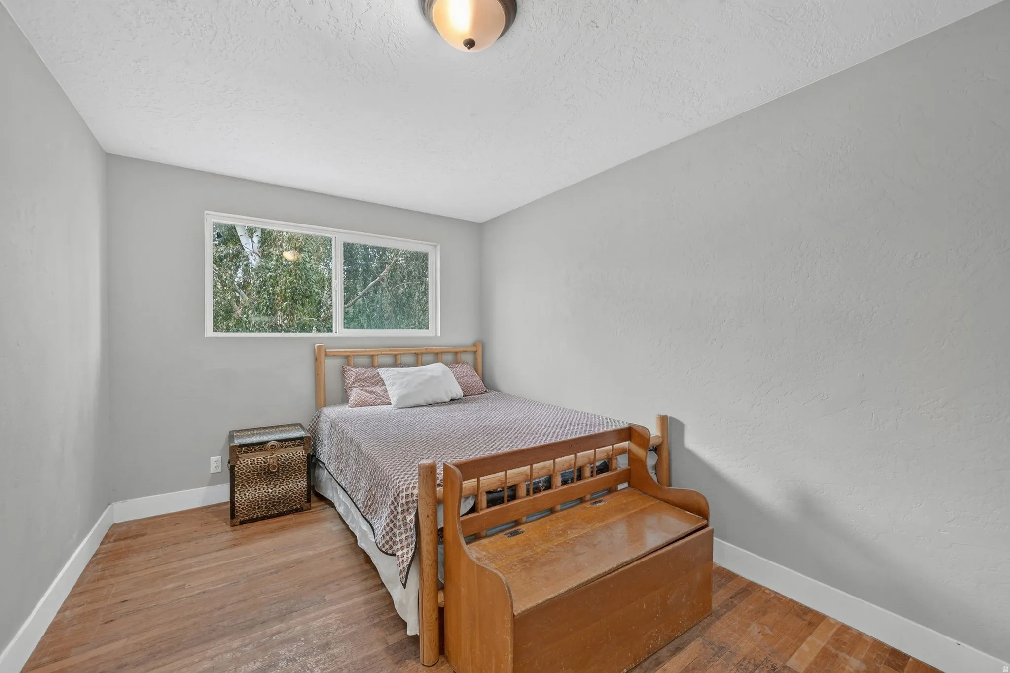 Window with exterior foliage, wood-finish flooring, and light gray wall finishes
