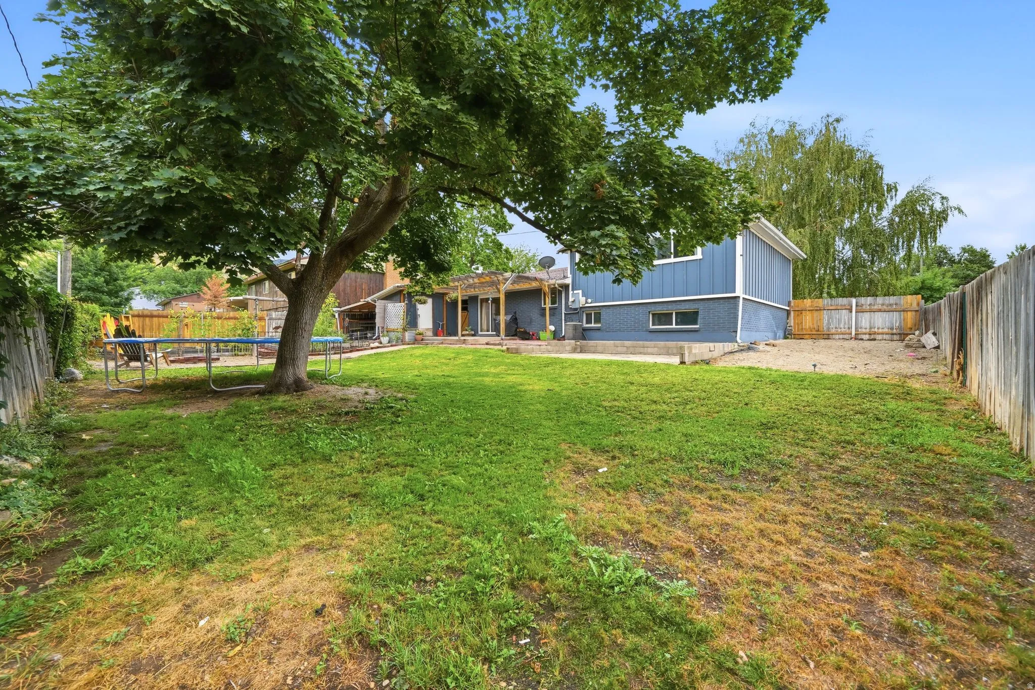 Expansive backyard with mature shade trees and lush lawn, fenced perimeter, and modern residential structures featuring blue exterior siding and updated architecture