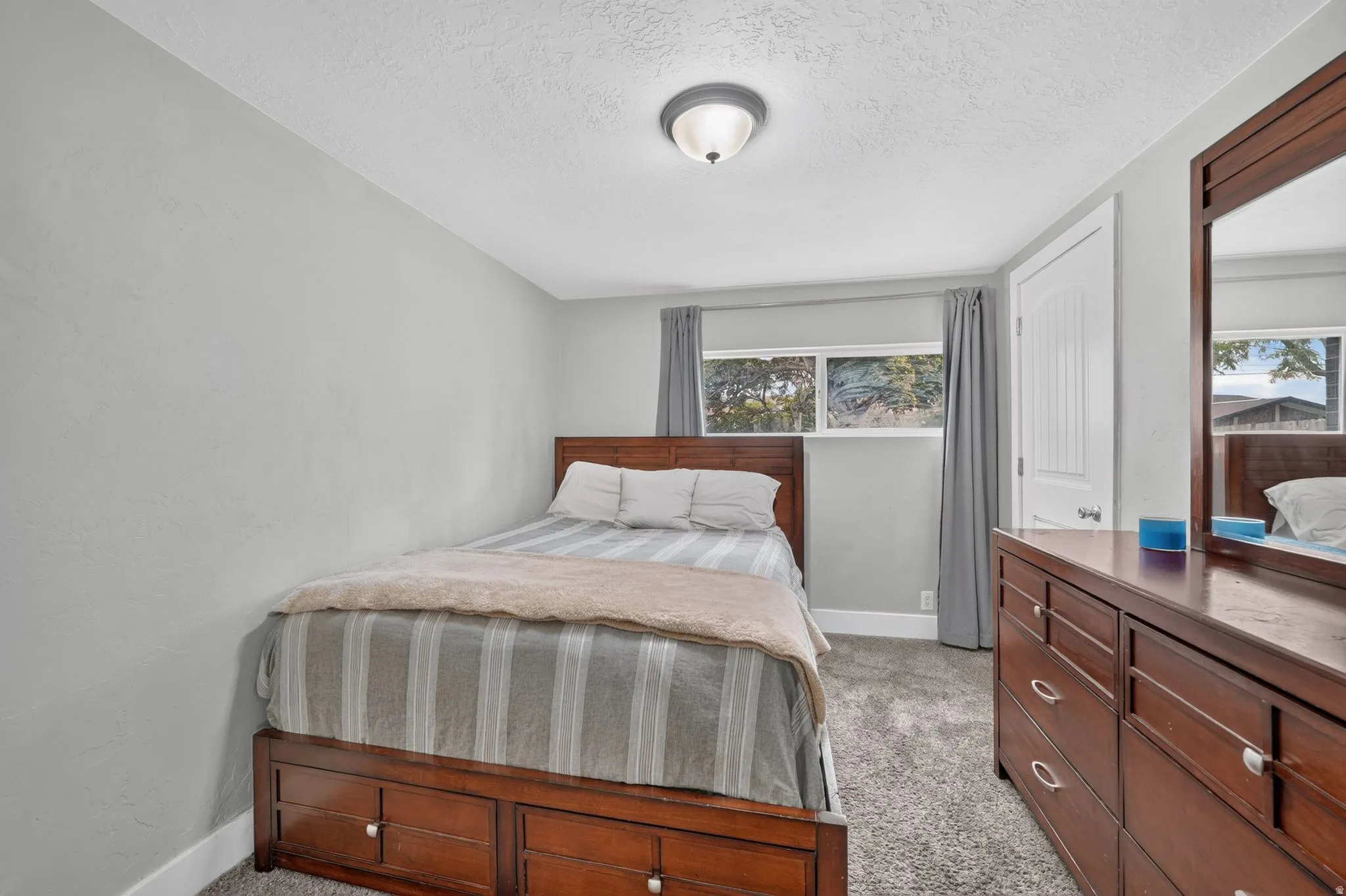 Bedroom featuring warm wood-finish furnishings, a striped upholstered bed frame, carpeted flooring, and dual windows with gray curtains