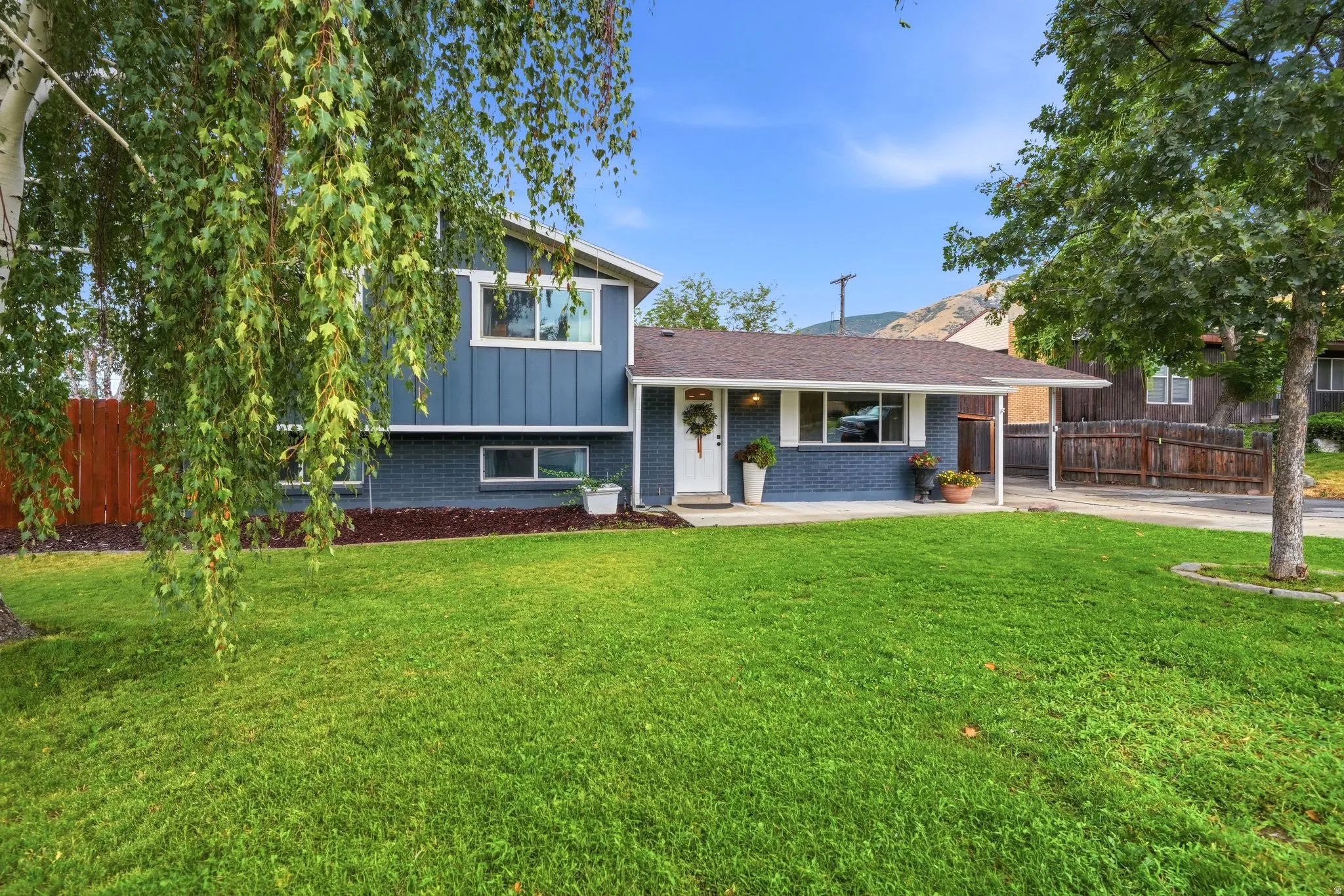 Charming mid-century home featuring a manicured lawn with mature trees, updated exterior with modern siding and roofing, covered front porch, and an attached garage with driveway access