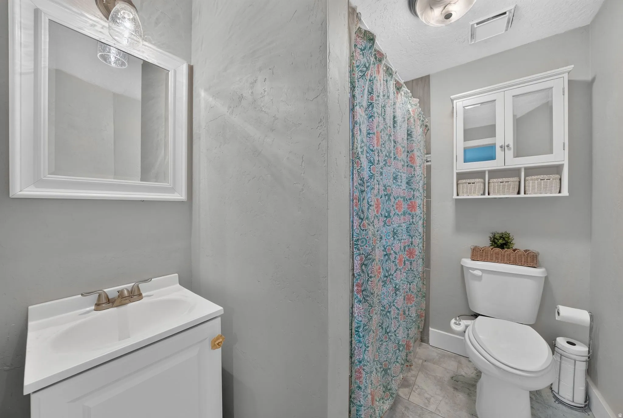 Compact bathroom featuring a white vanity sink, toilet, and tile flooring
