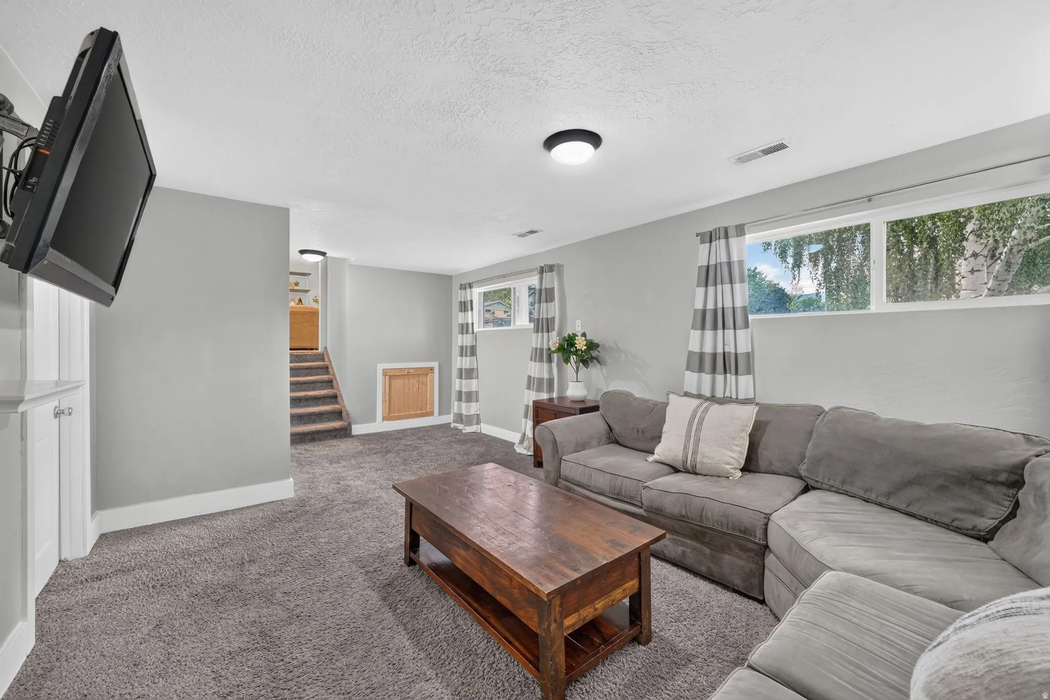Finished basement recreation room featuring plush sectional seating, wood-finish coffee table, recessed ceiling lighting, and abundant natural light from multiple windows
