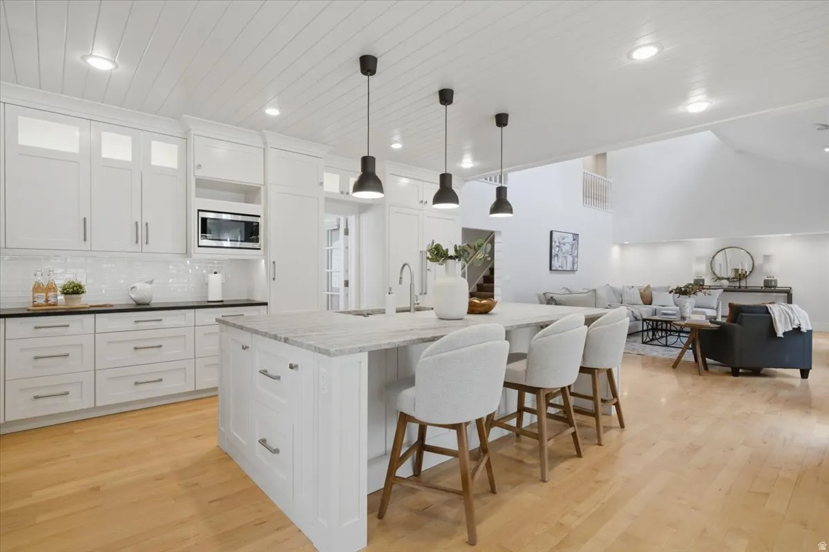 Kitchen featuring a large island with pendant lighting, white cabinetry, a tile backsplash, and wood-finish flooring