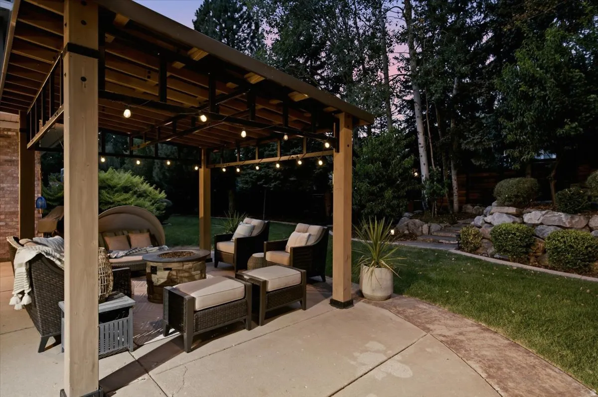 Expansive concrete patio with a wood-framed pergola, decorative string lights, and a rock retaining wall landscaping