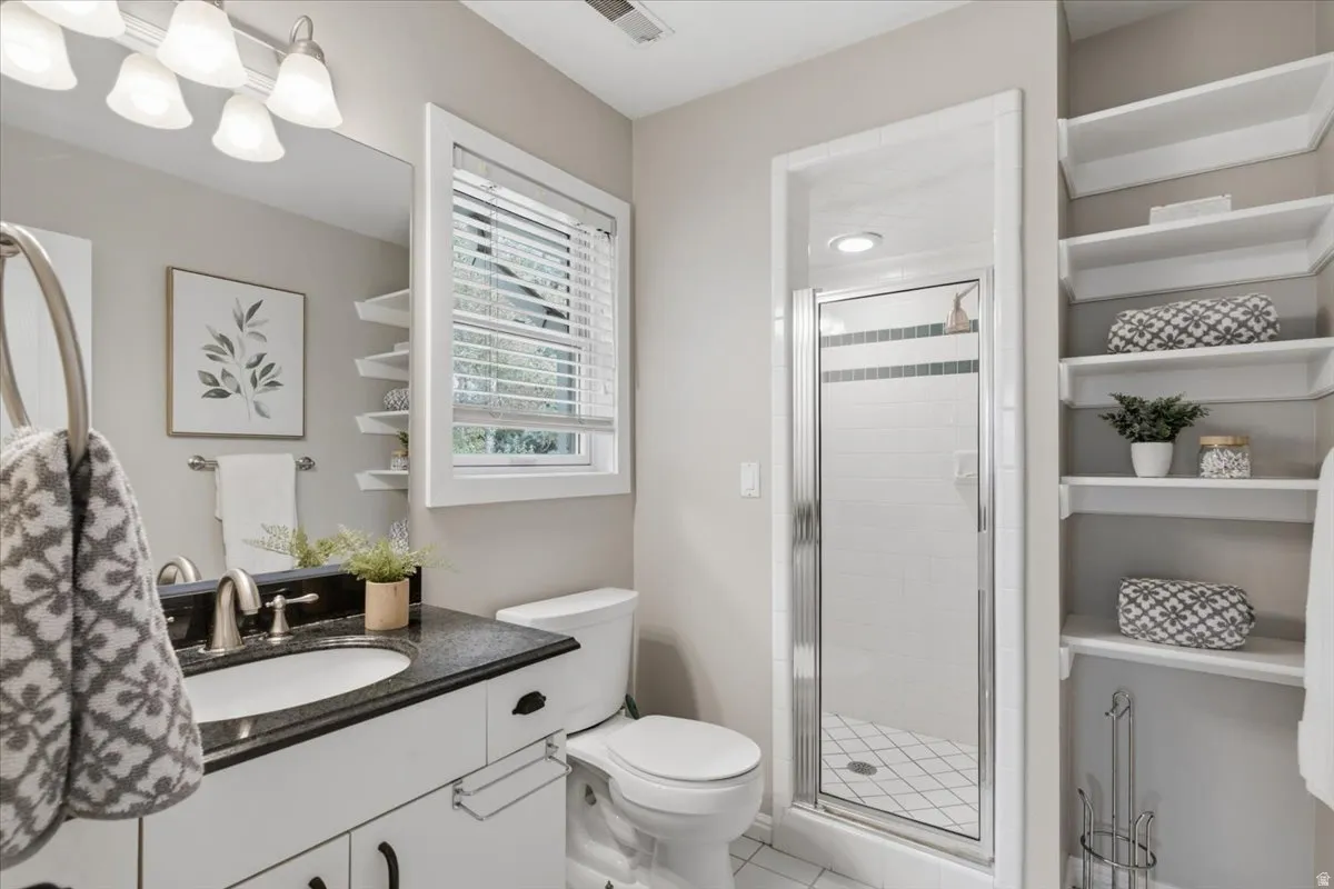 White vanity with dark countertop and undermount sink, mirrored wall, white window blinds, and built-in shelving