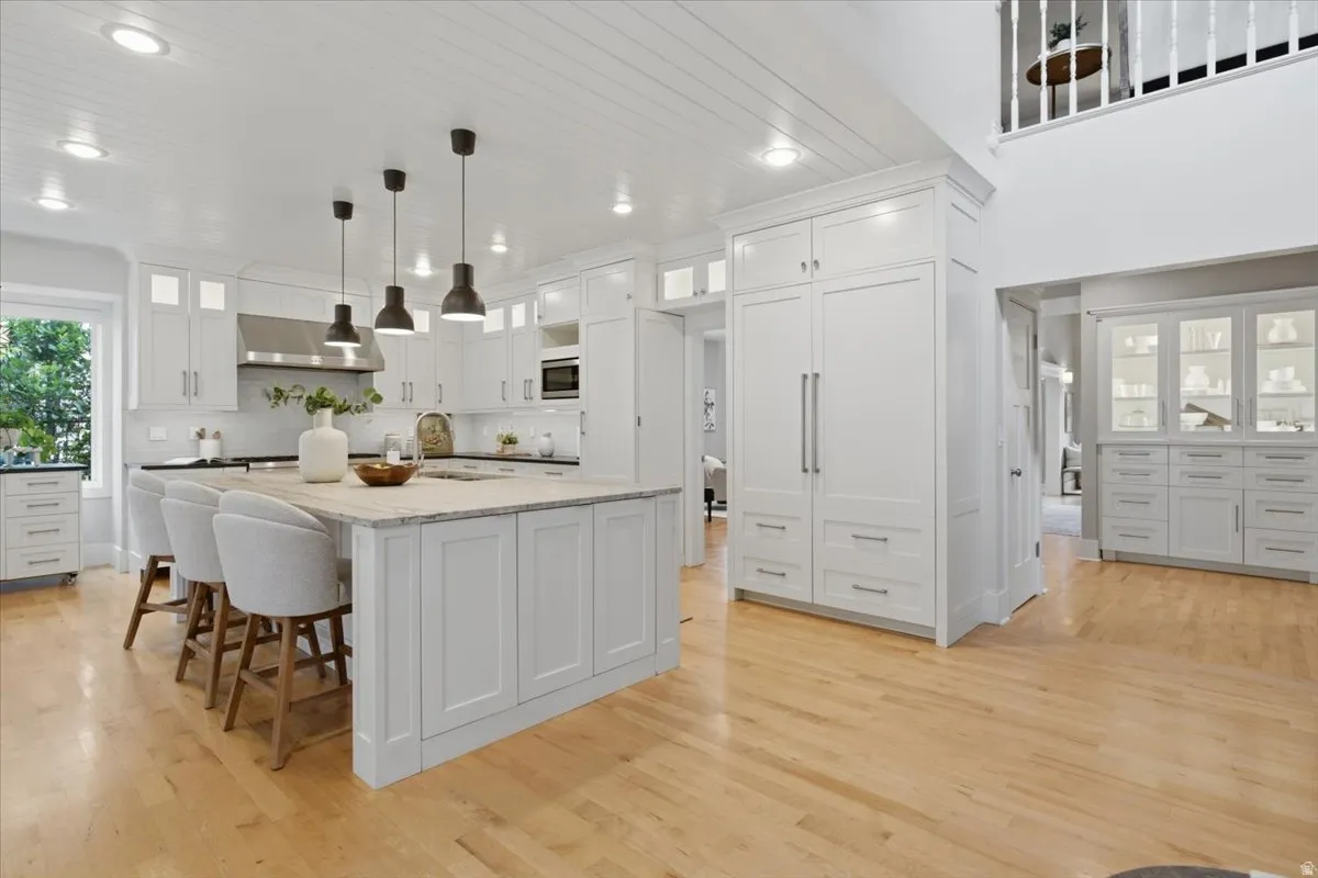 Gourmet kitchen featuring a large central island, white shaker cabinetry, hardwood flooring, integrated refrigeration, and a built-in microwave