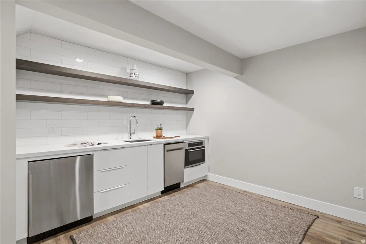 Full-size stainless steel refrigerator, white flat-panel cabinetry, integrated stainless steel dishwasher, built-in oven, and a white subway tile backsplash