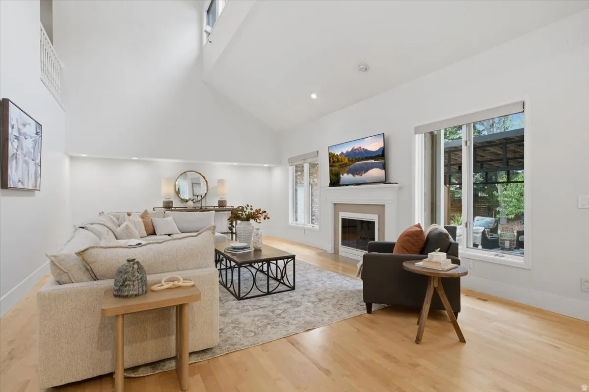 Vaulted ceilings, wood-finish flooring, a fireplace with a mantel, large windows, and recessed lighting