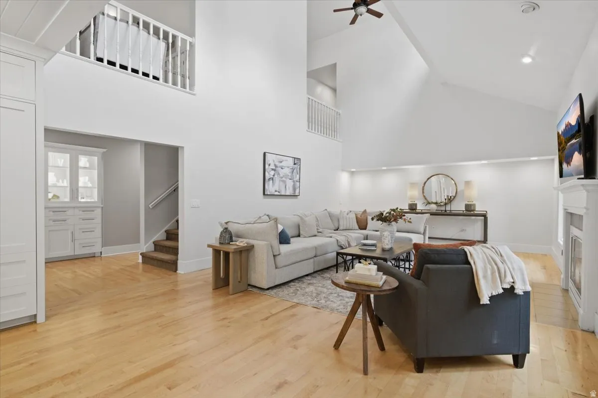 Vaulted ceiling with a ceiling fan, light wood-finish flooring, white fireplace, built-in display cabinetry, and an open loft area