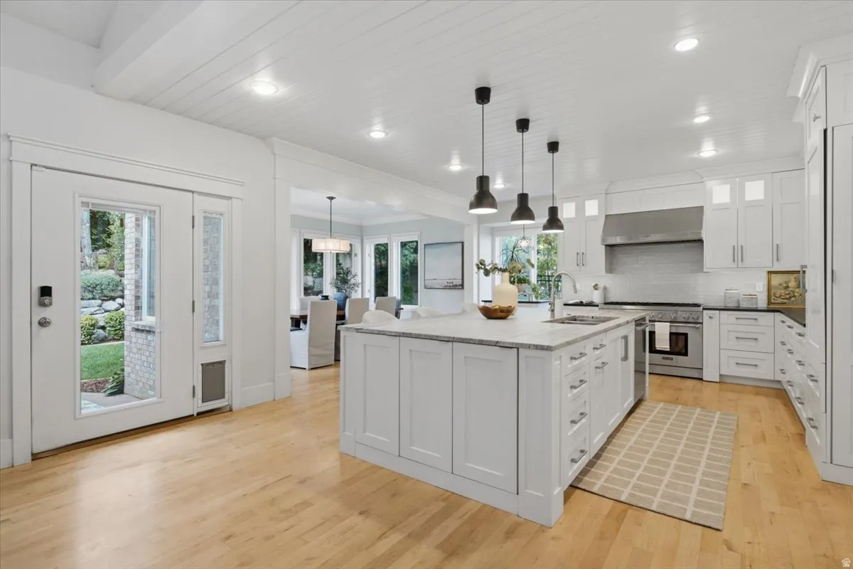 Kitchen featuring a large central island, light wood-finish flooring, white cabinetry, integrated stainless steel appliances, and ceiling-mounted pendant lighting