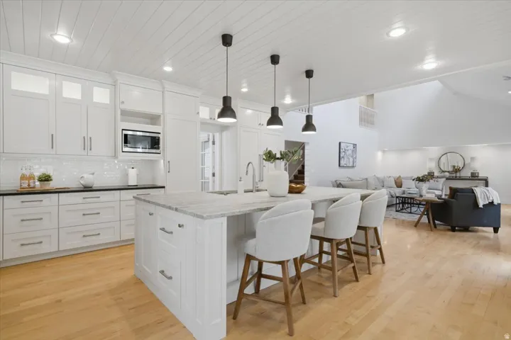 Kitchen featuring a large island with pendant lighting, white cabinetry, a tile backsplash, and wood-finish flooring
