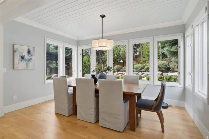 Wood-finish flooring, white shiplap ceiling, multiple large windows, and a chandelier with a drum shade
