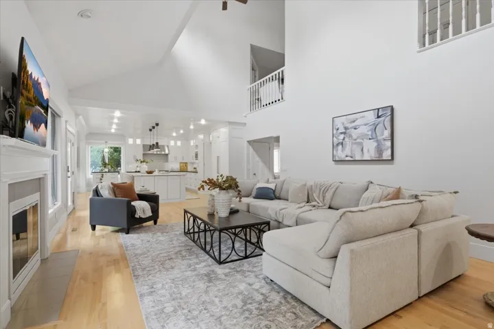 Vaulted ceilings, a fireplace with a white mantel, light wood-finish flooring, and a white kitchen with an island