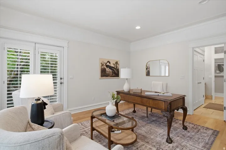 Wood-finish flooring, white plantation shutters, decorative crown molding, recessed lighting, and a doorway with white trim