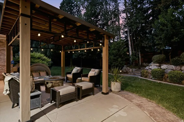 Expansive concrete patio with a wood-framed pergola, decorative string lights, and a rock retaining wall landscaping