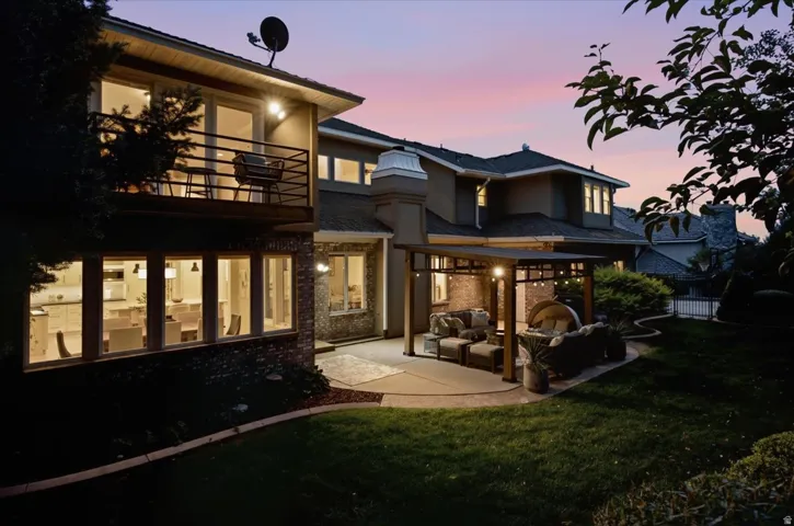 Extensive backyard with a manicured lawn, a large patio with a pergola, and a second-story balcony